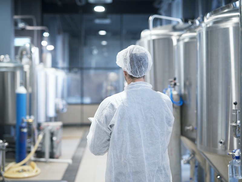 technologist in white protective suit walking through food factory production line checking quality.